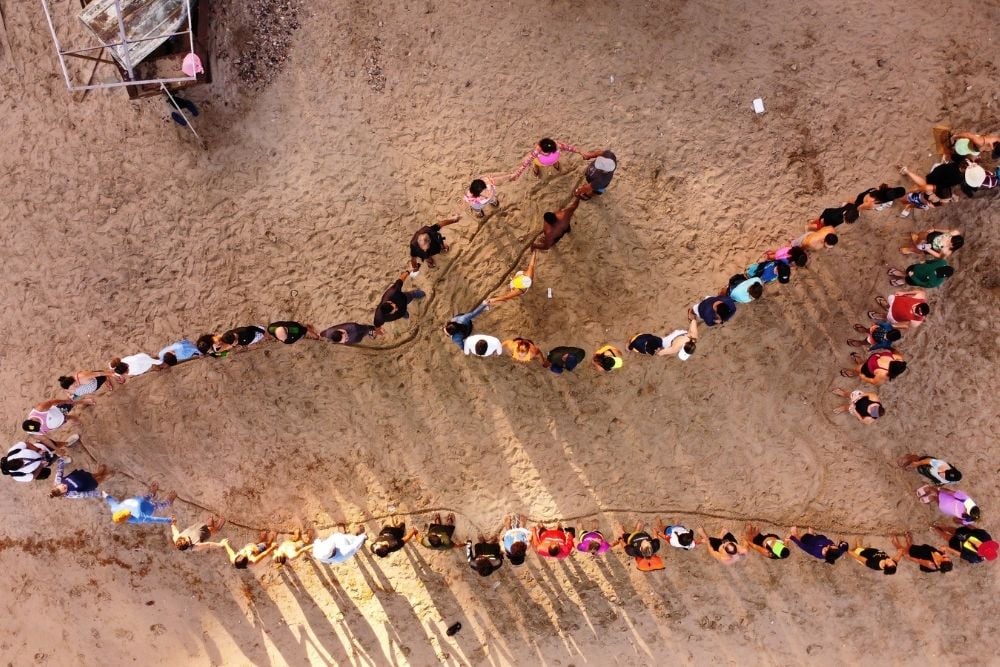 People on beach standing in the shape of a whale
