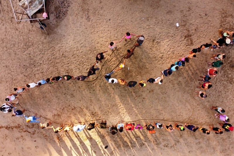 People on beach standing in the shape of a whale